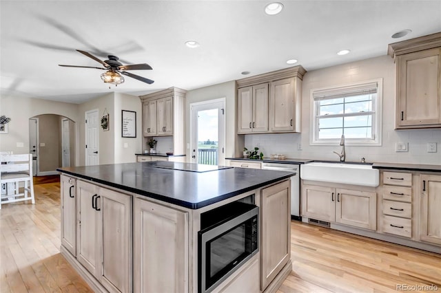 kitchen featuring appliances with stainless steel finishes, dark countertops, a sink, a ceiling fan, and arched walkways