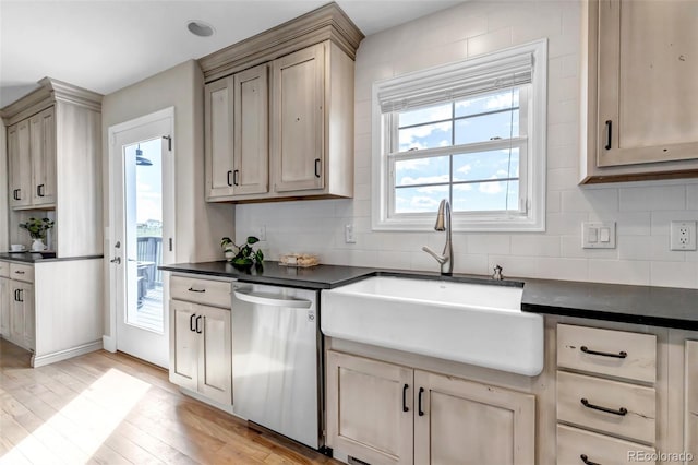 kitchen featuring stainless steel dishwasher, a sink, dark countertops, and light wood-style flooring