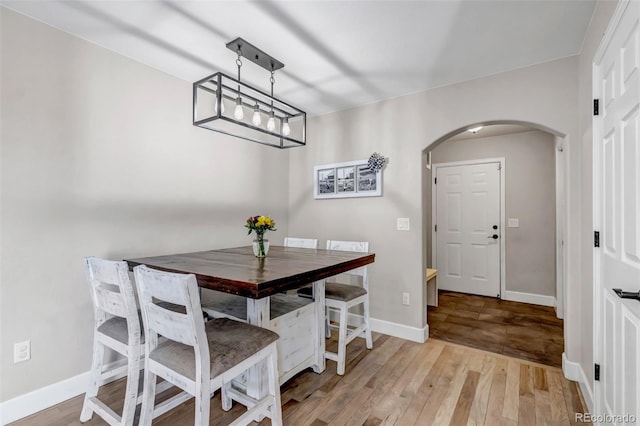 dining room featuring arched walkways, light wood-style floors, and baseboards