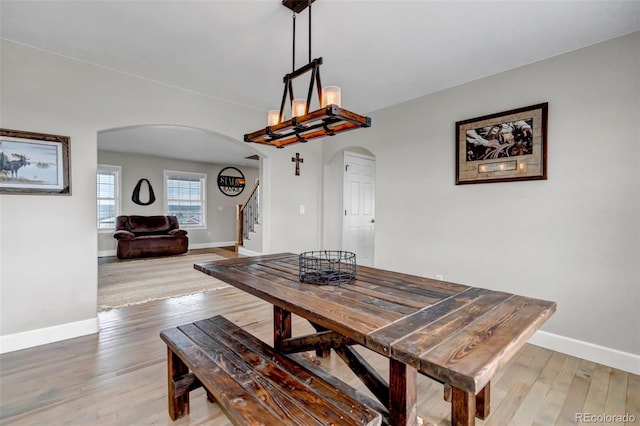 dining room featuring arched walkways, baseboards, stairs, and light wood-style flooring
