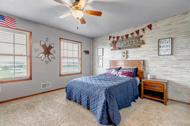 bedroom featuring baseboards, carpet floors, an accent wall, a ceiling fan, and wood walls