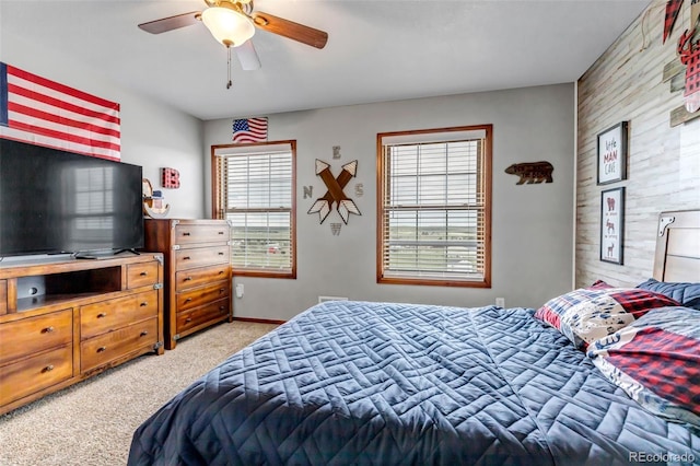 bedroom featuring light colored carpet, a ceiling fan, and an accent wall