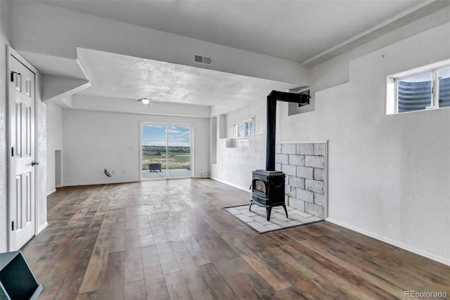 unfurnished living room featuring wood finished floors, a textured wall, baseboards, and a wood stove