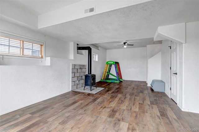 below grade area featuring a wood stove, wood finished floors, a ceiling fan, and a textured ceiling