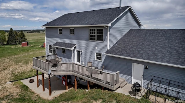 rear view of property with a wooden deck, a shingled roof, a lawn, and a patio area