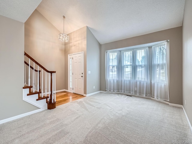 carpeted entryway featuring high vaulted ceiling, a chandelier, and a textured ceiling