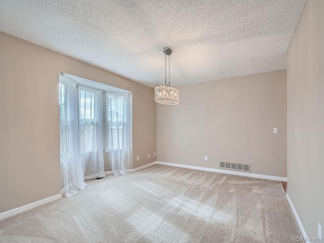 carpeted empty room featuring a textured ceiling and an inviting chandelier