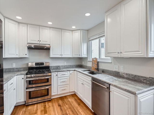 kitchen featuring appliances with stainless steel finishes, white cabinetry, sink, light stone countertops, and light hardwood / wood-style flooring