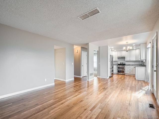 unfurnished living room with a textured ceiling, sink, light hardwood / wood-style flooring, and a notable chandelier