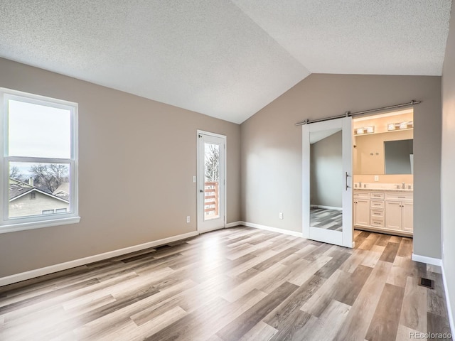 unfurnished bedroom featuring sink, light hardwood / wood-style flooring, vaulted ceiling, access to outside, and a barn door