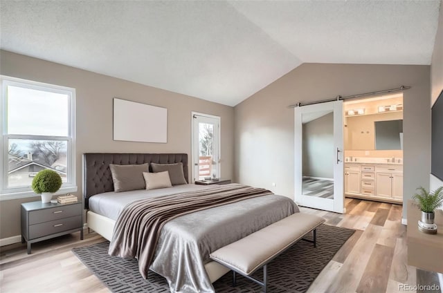 bedroom with lofted ceiling, sink, ensuite bath, a barn door, and light wood-type flooring