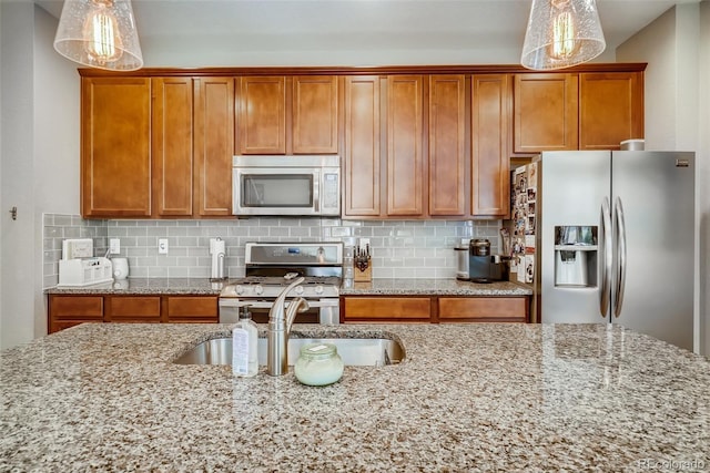 kitchen featuring appliances with stainless steel finishes, sink, hanging light fixtures, and light stone countertops