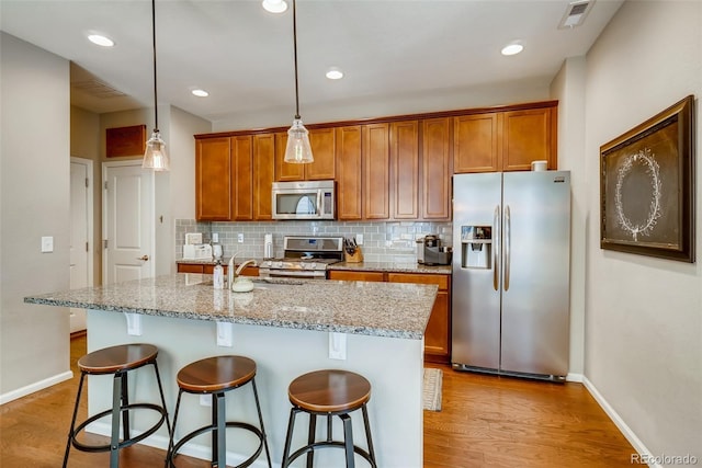 kitchen featuring decorative light fixtures, decorative backsplash, stainless steel appliances, and an island with sink