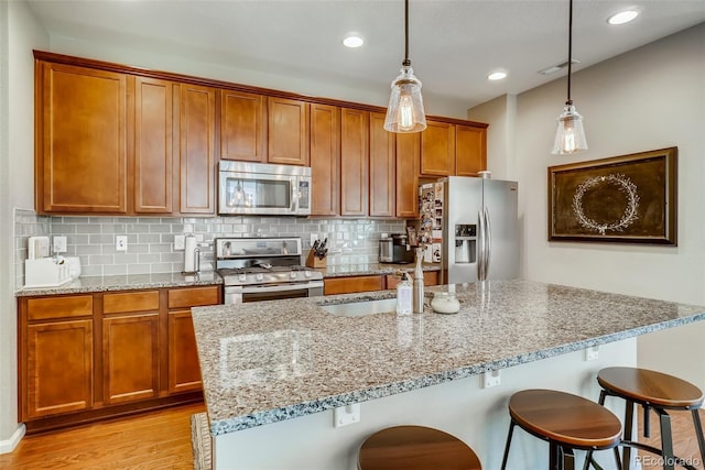 kitchen with pendant lighting, stainless steel appliances, decorative backsplash, light stone counters, and a breakfast bar