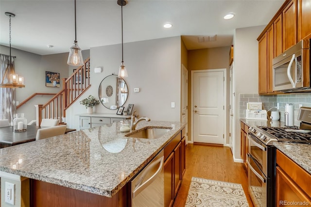 kitchen with light stone countertops, pendant lighting, stainless steel appliances, sink, and a center island with sink