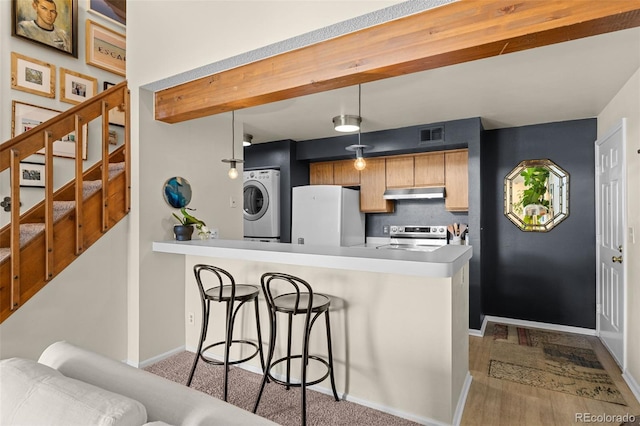 kitchen featuring stainless steel electric range, visible vents, freestanding refrigerator, under cabinet range hood, and a kitchen bar