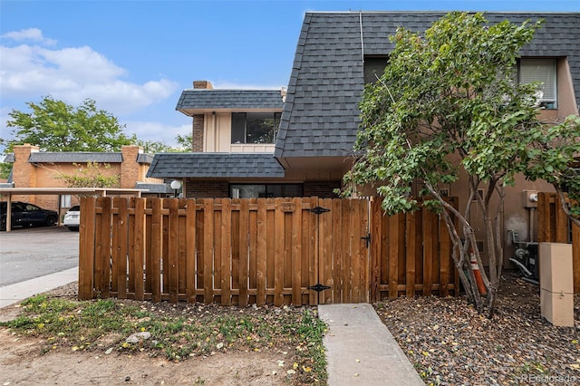 exterior space featuring brick siding, fence, mansard roof, and roof with shingles