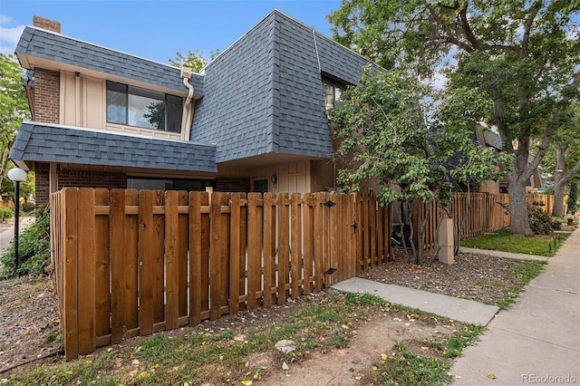 view of property exterior featuring brick siding, a fenced front yard, mansard roof, and roof with shingles