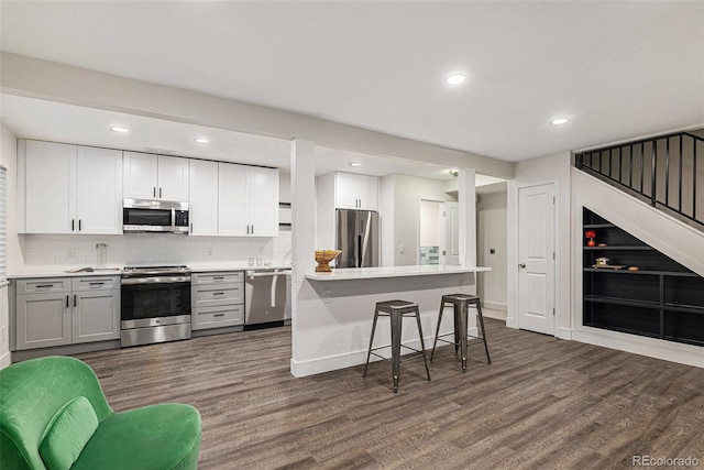 kitchen with dark wood finished floors, stainless steel appliances, light countertops, and a kitchen breakfast bar