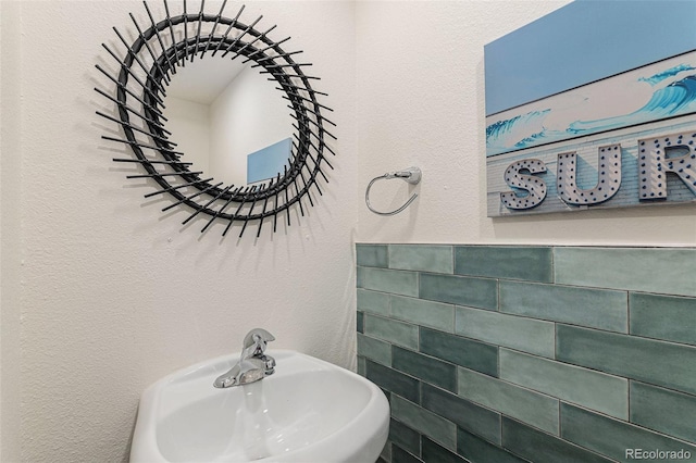 bathroom with a textured wall, a sink, and tile walls