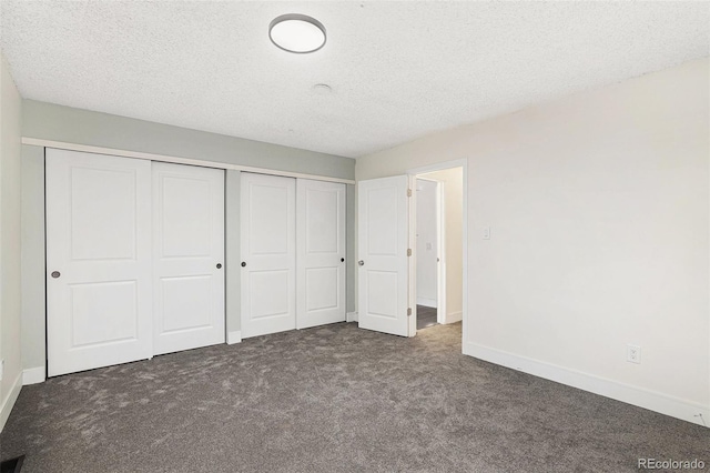 unfurnished bedroom featuring baseboards, a closet, dark carpet, and a textured ceiling