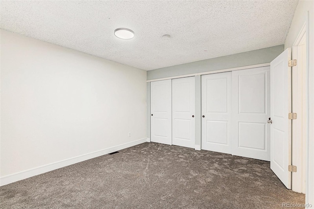 unfurnished bedroom featuring baseboards, dark carpet, and a textured ceiling