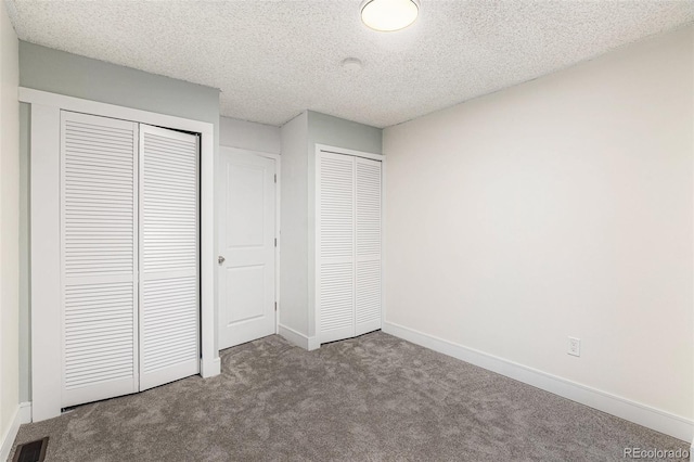 unfurnished bedroom featuring a textured ceiling, carpet floors, visible vents, baseboards, and two closets