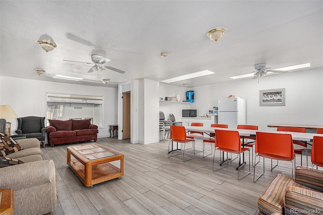 living room with a ceiling fan, light wood-style floors, a textured ceiling, and baseboards