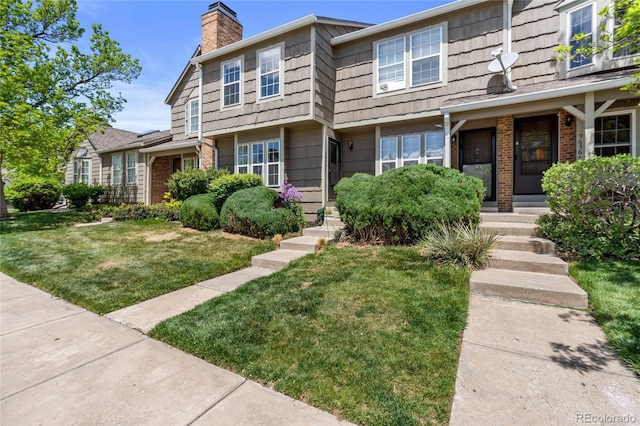 multi unit property with a front yard, a chimney, and brick siding