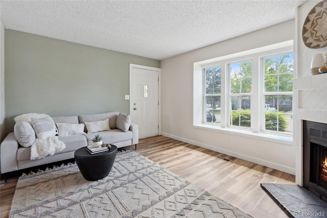 living room featuring a warm lit fireplace, wood finished floors, a textured ceiling, and baseboards