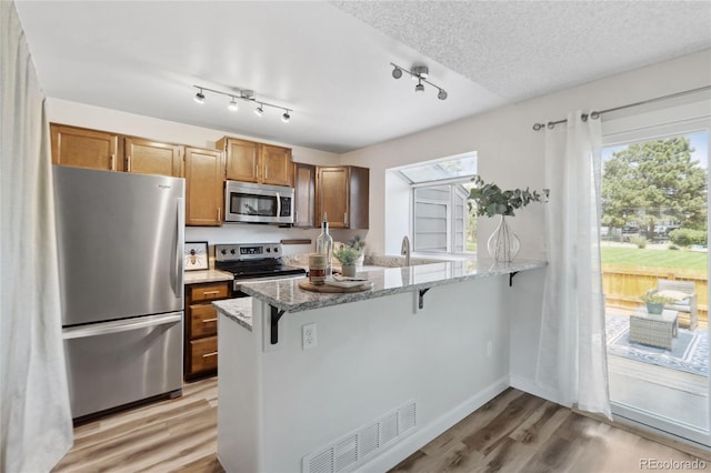 kitchen featuring appliances with stainless steel finishes, a peninsula, a breakfast bar area, light wood-type flooring, and light stone countertops