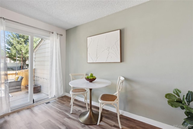 dining room featuring a textured ceiling, wood finished floors, and baseboards