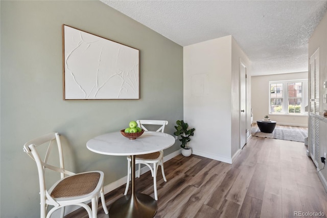 dining room with wood finished floors, a textured ceiling, and baseboards