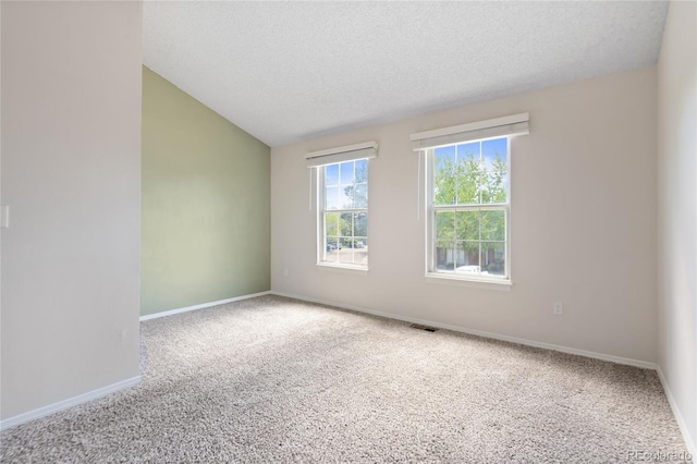 carpeted empty room featuring vaulted ceiling, baseboards, and a textured ceiling