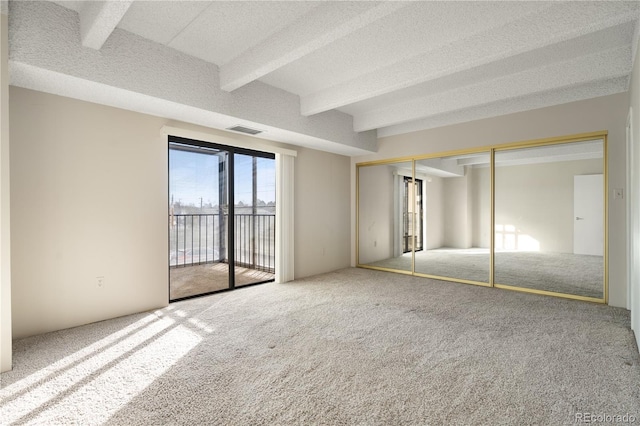 unfurnished bedroom featuring beam ceiling, carpet flooring, a textured ceiling, access to outside, and a closet