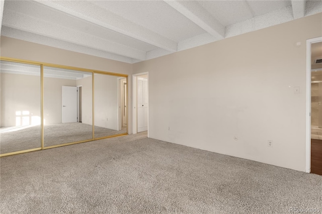 unfurnished bedroom featuring beamed ceiling, carpet, and a closet