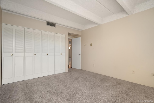 unfurnished bedroom with beamed ceiling, carpet floors, and a closet