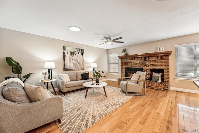 living room with ceiling fan, hardwood / wood-style flooring, a brick fireplace, and a healthy amount of sunlight