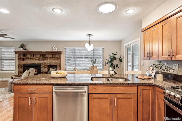 kitchen featuring a fireplace, sink, dark stone counters, appliances with stainless steel finishes, and pendant lighting