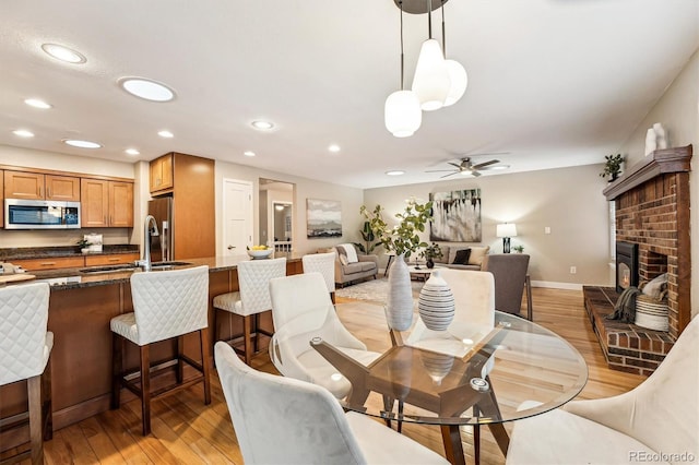 dining space featuring a brick fireplace, light hardwood / wood-style floors, sink, and ceiling fan