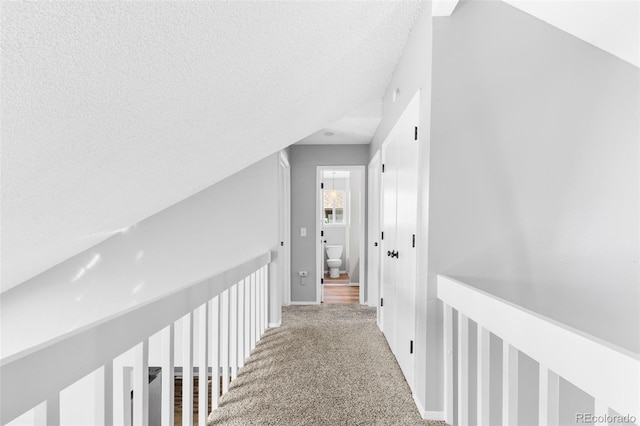 hall featuring carpet, a textured ceiling, and vaulted ceiling