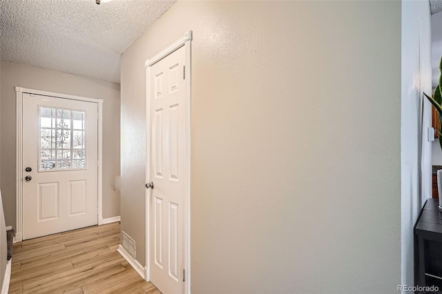 entryway with light wood-style flooring, a textured ceiling, and baseboards