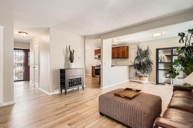 living area featuring visible vents, baseboards, a textured ceiling, and light wood-style flooring