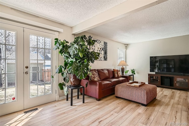 living area featuring plenty of natural light, wood finished floors, visible vents, and french doors