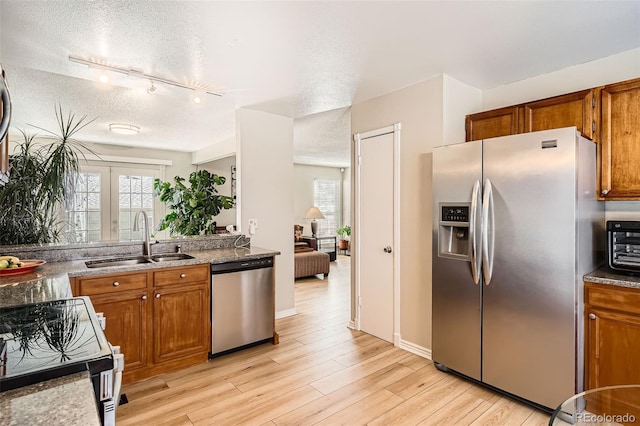 kitchen with brown cabinetry, light wood finished floors, appliances with stainless steel finishes, and a sink