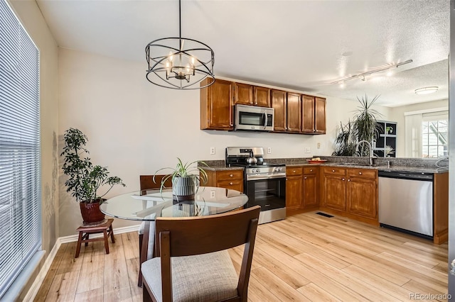 kitchen featuring light wood finished floors, a chandelier, stainless steel appliances, a textured ceiling, and a sink