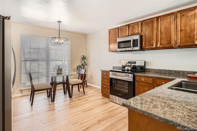 kitchen featuring brown cabinets, appliances with stainless steel finishes, pendant lighting, and light wood-type flooring