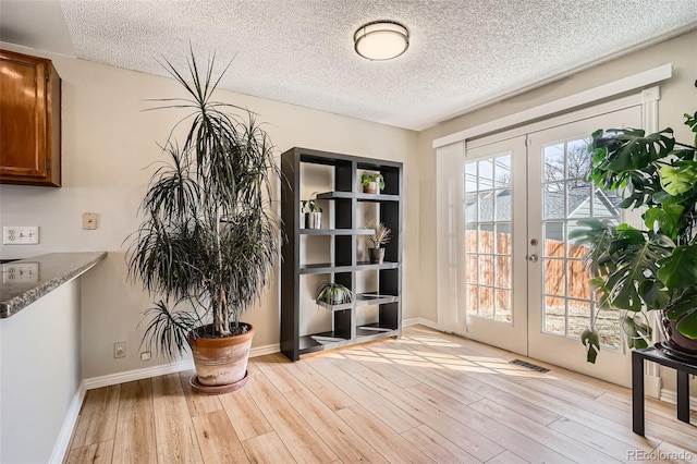 interior space with visible vents, light wood-style flooring, a textured ceiling, french doors, and baseboards