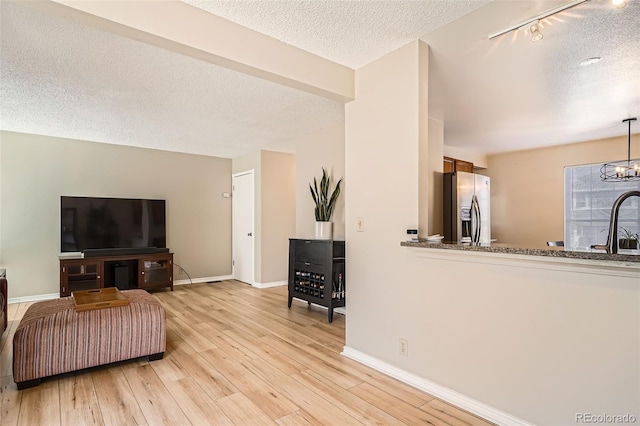 living area featuring a textured ceiling, light wood-style floors, baseboards, and a chandelier