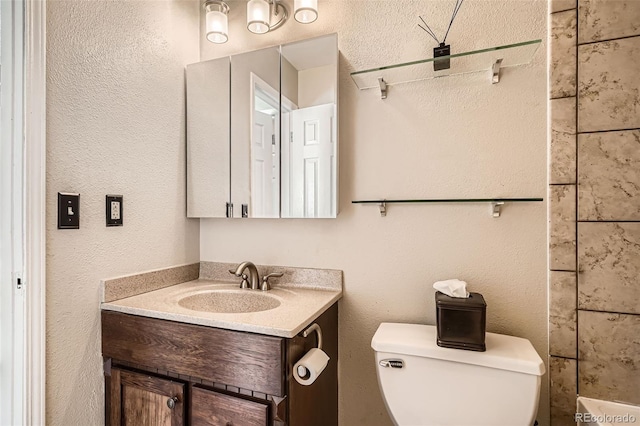 full bath featuring vanity, toilet, and a textured wall